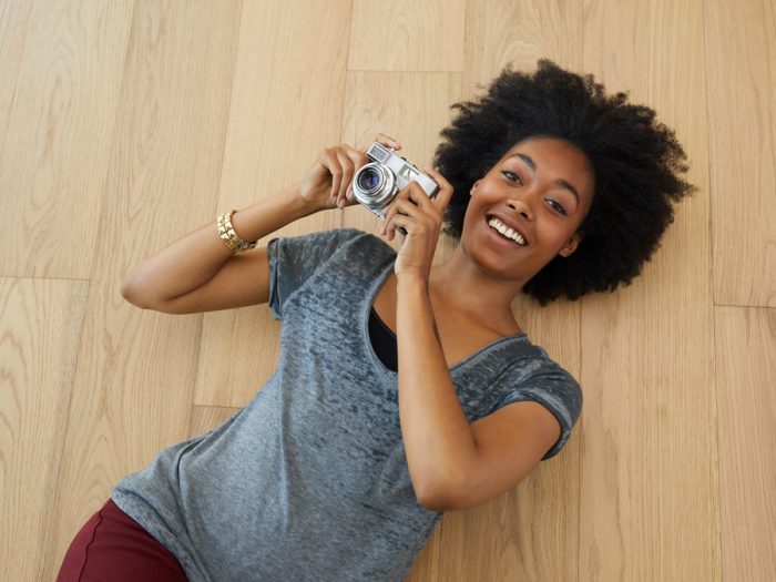 African American woman laying on hardwood floor, smiling, and holding a camera