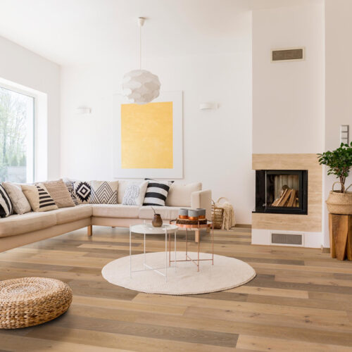 hardwood floor in white living room with a couch, rug, table, artwork,fireplace, windows, and stairs leading to second floor