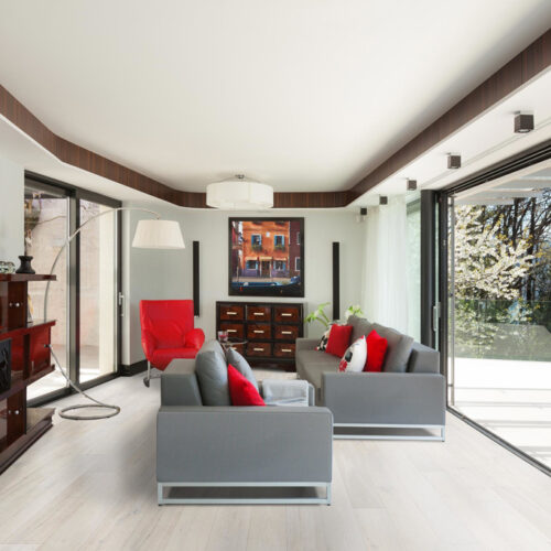 hardwood floors in TV room with two gray couches, TV, lamp, brown cabinets, and large window with the woods and lake beyond