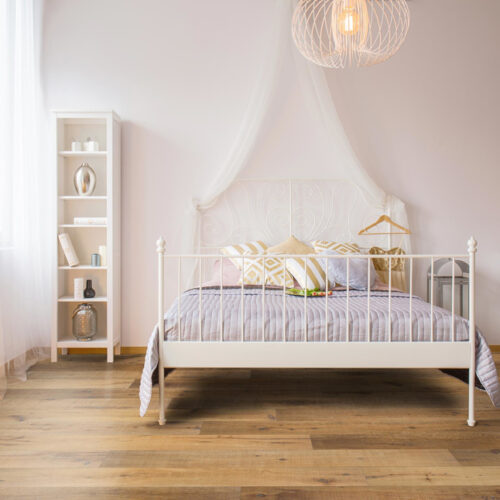 hardwood floor in white furnished bedroom with bed, bookcase, and drawers