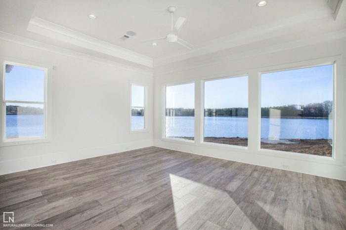 hardwood floor in empty, white room with five windows overlooking a lake and beach