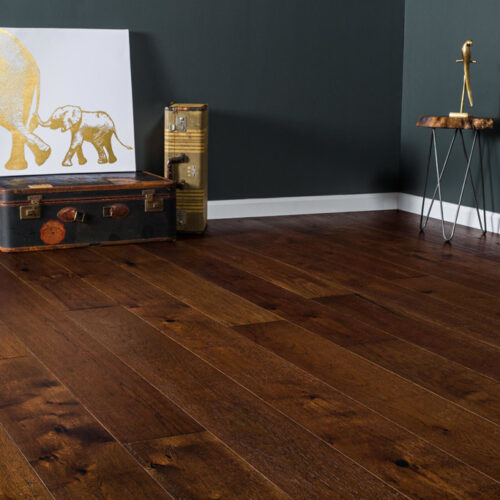 hardwood floors in corner of room with trunk, suitcase, elephant painting, and table