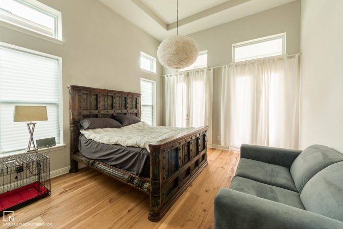 hardwood floors in bedroom with bed, couch, lamp, and dog crate