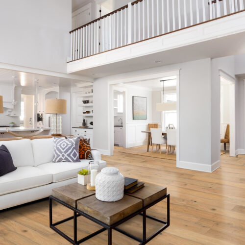 hardwood flooring in a living room with white furniture and dining room and kitchen visible in background