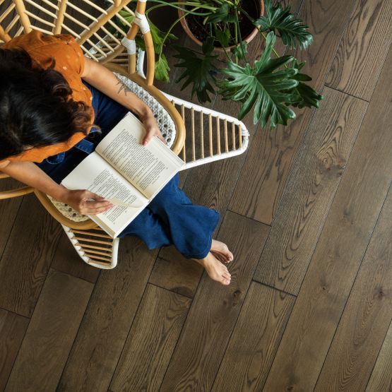 high angle view of a room with hardwood flooring and a woman sitting in a chair reading a book with a large plant next to her