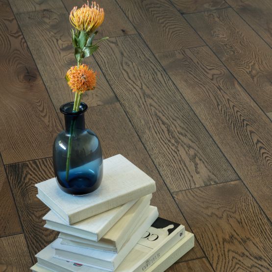 hardwood flooring and white books stacked on the fllor with a blue glass vase holding two flowers