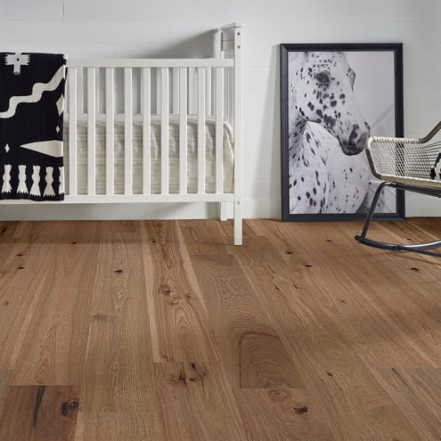 hardwood flooring in baby nursery with black and white decor, crib, blanket, rocking chair and painting of a horse