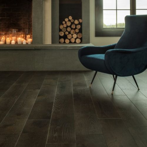 hardwood flooring with a chair next to a fireplace filled with candles and stacked logs next to it