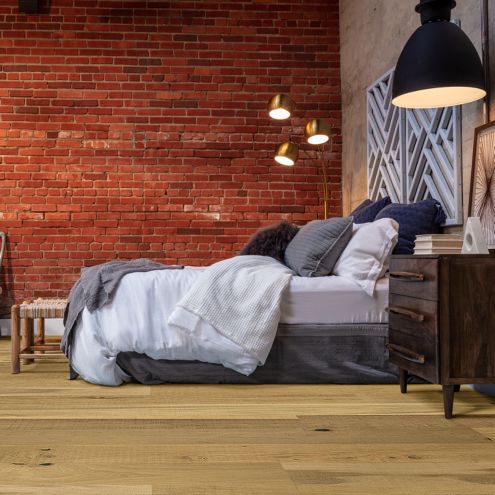 hardwood flooring in industrial bedroom with a bed, end table, lamps, painting, and a red brick wall