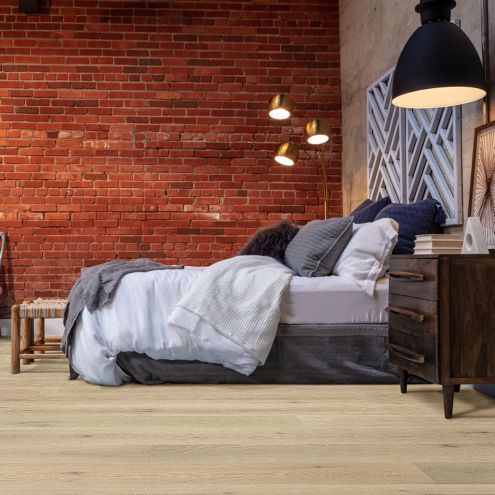 hardwood flooring in industrial bedroom with a bed, end table, lamps, painting, and a red brick wall