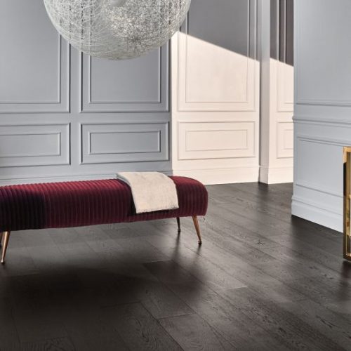 hardwood flooring in a white room with a burgundy colored upholstered bench and a thin, white folded material on it.