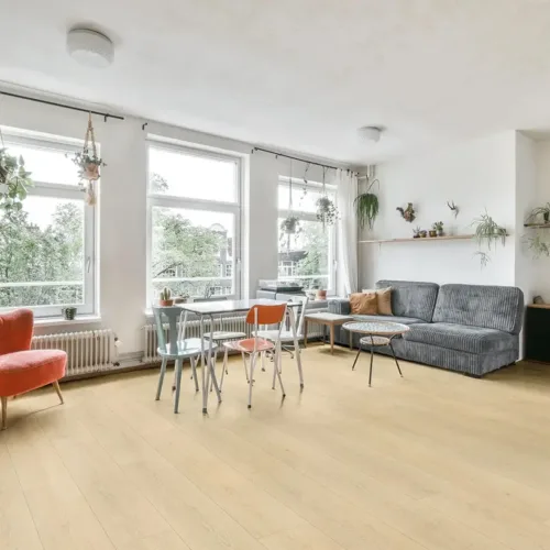 Nantucket pale blonde waterproof luxury vinyl plank flooring in a sunny living room with red chairs and grey sofa
